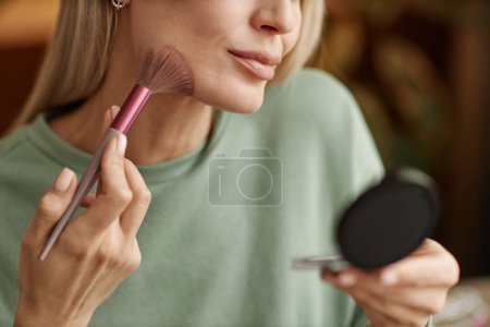 Foto de Primer plano de la mujer adulta haciendo maquillaje mirando en espejo compacto y aplicando contorno con espacio de copia de cepillo de cosméticos - Imagen libre de derechos