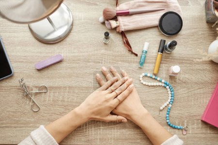 Photo for Top view closeup of elegant female hands with fresh manicure and golden rings resting on vanity table with makeup and womens accessories copy space - Royalty Free Image