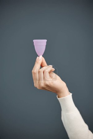 Téléchargez les photos : Plan vertical de la main féminine tenant la coupe menstruelle en silicone rose sur fond bleu espace de copie - en image libre de droit