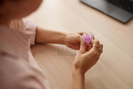 Photo for Top view closeup of unrecognizable woman folding menstrual cup sitting at table with laptop copy space - Royalty Free Image