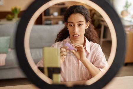 Foto de Vista frontal de una mujer joven sosteniendo videos de grabación de copa menstrual a través de un teléfono inteligente con luz de anillo - Imagen libre de derechos