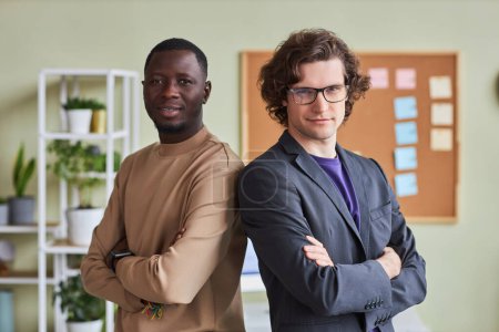 Photo for Waist up portrait of two young men in office posing confidently with arms crossed and looking at camera - Royalty Free Image