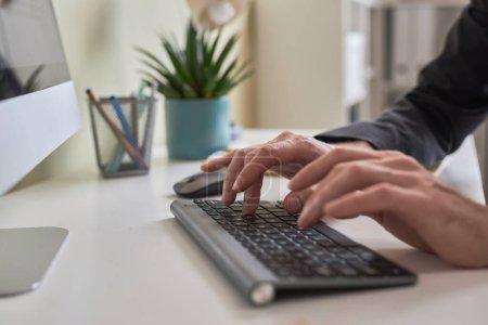 Téléchargez les photos : Gros plan des mains masculines tapant sur le clavier sans fil tout en utilisant l'ordinateur sur le lieu de travail de bureau, espace de copie - en image libre de droit