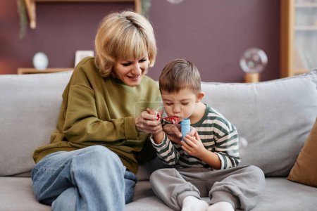 Photo for Front view portrait of mother and son with down syndrome blowing bubbles while sitting on sofa at home - Royalty Free Image