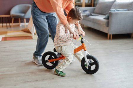 Photo for Side view portrait of little boy with down syndrome playing with runbike mom assisting - Royalty Free Image