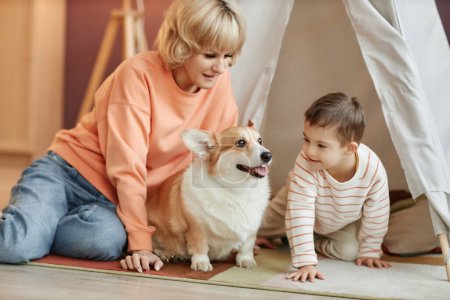 Petit garçon avec le syndrome du duvet jouant avec maman et chien à la maison dans une tente de jeux confortable