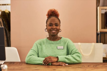 Téléchargez les photos : Portrait de la femme noire souriante regardant la caméra au comptoir travaillant dans un magasin de vêtements, espace de copie - en image libre de droit