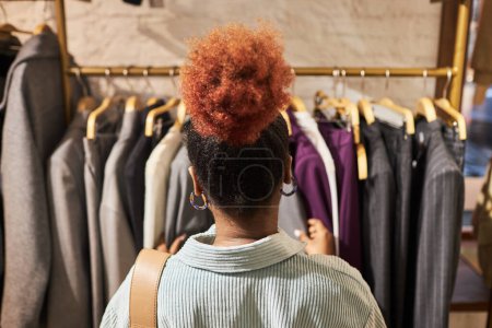 Foto de Vista posterior primer plano de la joven mujer negra que navega por la ropa en los bastidores en la tienda de ropa, espacio de copia - Imagen libre de derechos