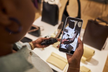 Téléchargez les photos : Gros plan de la jeune femme prenant des photos de chaussures dans la boutique de vêtements via smartphone - en image libre de droit