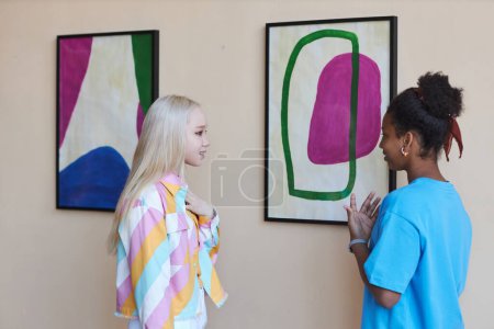 Foto de Retrato de vista lateral mínima de dos chicas adolescentes discutiendo imágenes en la galería de arte moderno - Imagen libre de derechos