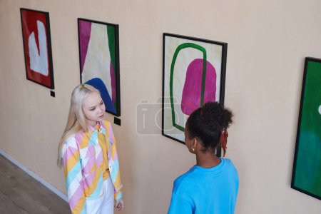 Foto de Vista de ángulo alto de dos chicas adolescentes hablando mientras visitan la galería de arte moderno o el museo, espacio para copiar - Imagen libre de derechos
