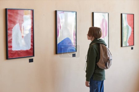 Téléchargez les photos : Portrait minimal d'un adolescent regardant de l'art abstrait sur un mur dans une galerie d'art ou un musée, espace de copie - en image libre de droit