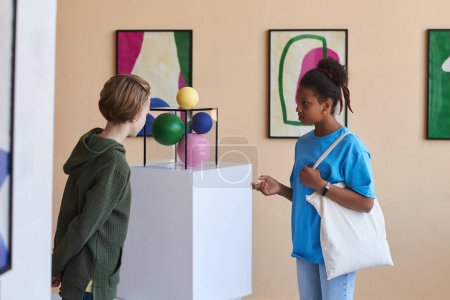 Téléchargez les photos : Portrait coloré de deux adolescents regardant abréger la sculpture dans la galerie d'art moderne - en image libre de droit