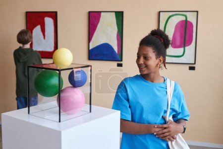 Foto de Colorido retrato de una adolescente sonriente mirando abstraer la escultura en la galería de arte moderno - Imagen libre de derechos
