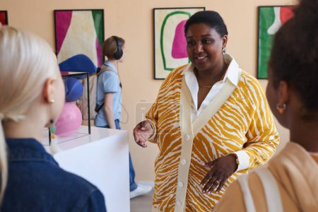 Téléchargez les photos : Groupe diversifié d'adolescents écoutant une enseignante dans une galerie d'art moderne ou un musée - en image libre de droit
