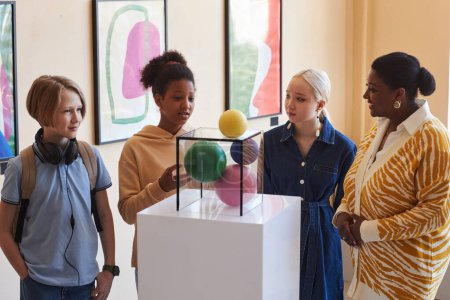 Téléchargez les photos : Groupe diversifié d'écoliers écoutant un enseignant ou un guide touristique en regardant des sculptures - en image libre de droit