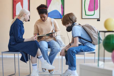 Foto de Grupo de tres adolescentes sentados en círculo haciendo proyecto escolar en galería de arte moderno o museo - Imagen libre de derechos
