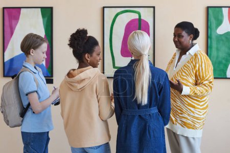 Téléchargez les photos : Groupe diversifié d'écoliers adolescents écoutant un guide féminin dans une galerie d'art moderne - en image libre de droit