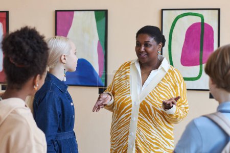 Photo for Waist up portrait of overweight black woman giving tour to group of teenagers in art gallery - Royalty Free Image