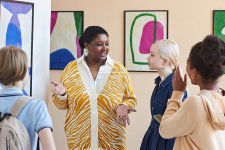 Foto de Retrato en la cintura de una mujer negra sonriente con un grupo de adolescentes en una galería de arte o museo - Imagen libre de derechos