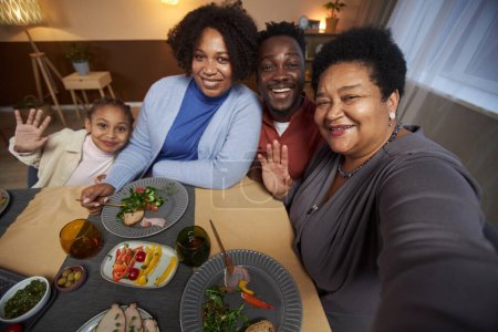 Téléchargez les photos : Portrait de grande famille afro-américaine prenant selfie photo à table ensemble et agitant avec grand-mère tenant caméra - en image libre de droit