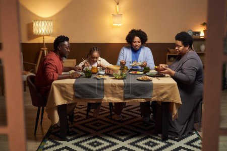 Téléchargez les photos : Portrait complet d'une grande famille afro-américaine assise à table et mangeant des photos à travers des portes ouvertes - en image libre de droit