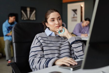Porträt einer jungen Frau am Computer im Büro mit neutralem Gesichtsausdruck und Händchen haltend