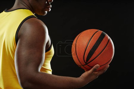 Foto de Vista lateral de primer plano de jugador de baloncesto afroamericano sosteniendo la pelota contra fondo negro con espacio de copia - Imagen libre de derechos