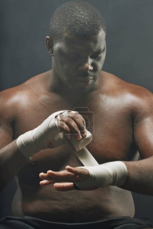 Foto de Retrato vertical dramático de boxeador envolviendo las manos con vendas preparándose para la lucha contra el fondo negro - Imagen libre de derechos