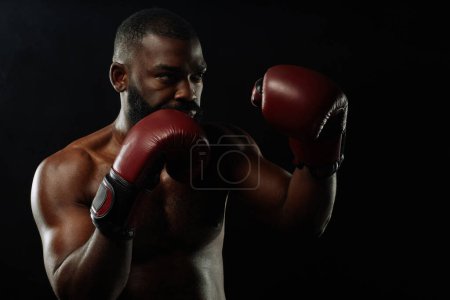 Téléchargez les photos : Dramatique tir à basse lumière de boxeur afro-américain en position de combat sur fond noir - en image libre de droit