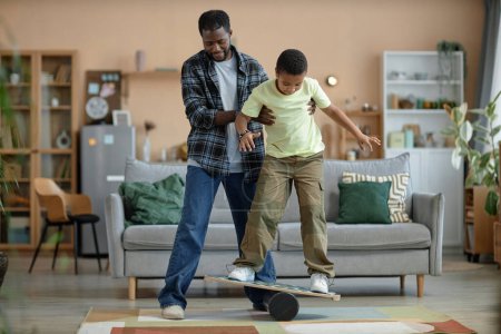 Foto de Retrato completo del padre afroamericano enseñando a su hijo de pie en el tablero de equilibrio - Imagen libre de derechos