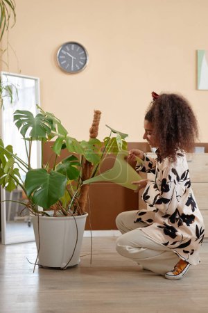 Téléchargez les photos : Portrait vertical pleine longueur de jeune femme prenant soin de grande plante d'intérieur en pot à l'espace de copie à la maison - en image libre de droit