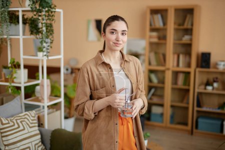 Téléchargez les photos : Portrait à la taille d'une jeune femme tenant un arrosoir en verre et souriant à la caméra à la maison espace de copie - en image libre de droit