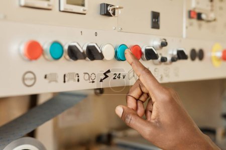 Closeup of black young man using control panel at factory focus on hand pushing button, copy space