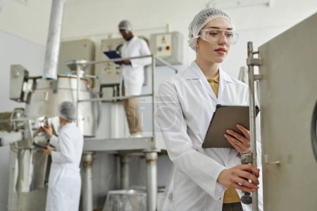 Foto de Retrato de cintura hacia arriba de una mujer joven que usa equipo operativo de bata de laboratorio en el taller de fábrica farmacéutica, espacio de copia - Imagen libre de derechos
