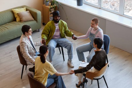 Foto de Vista de ángulo alto del grupo de personas cogidas de la mano mientras están sentadas en la sesión de psicoterapia - Imagen libre de derechos