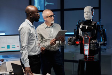 Foto de Dos ingenieros multiétnicos examinan el programa de robot usando tableta digital mientras están en la oficina - Imagen libre de derechos