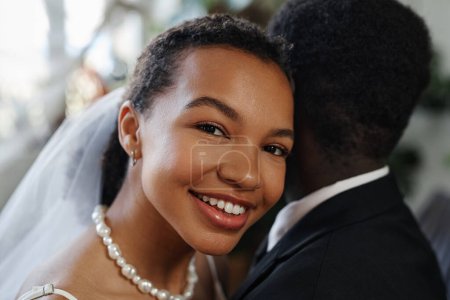 Photo for Close up portrait of black young woman smiling at camera laying head on grooms shoulder in wedding ceremony - Royalty Free Image
