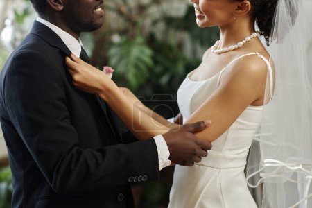 Foto de Vista lateral primer plano de pareja joven negro casarse con novia ajustando chaqueta y boutonniere antes de la ceremonia de boda - Imagen libre de derechos