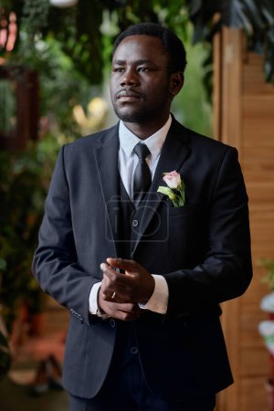 Foto de Retrato vertical del guapo hombre negro preparándose para la ceremonia de boda y ajustando el esmoquin - Imagen libre de derechos