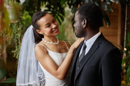 Téléchargez les photos : Portrait taille haute de jeune couple noir se mariant et se regardant avec amour posant ensemble dans l'orangerie verte - en image libre de droit