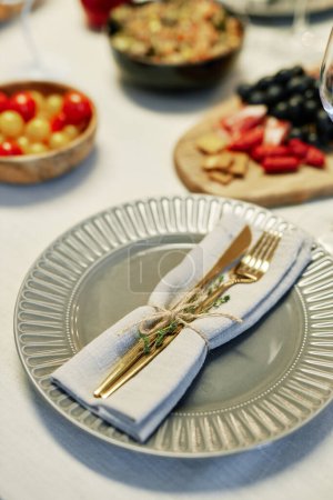 Photo for Focus on grey plate with folded cotton or linen napkin and fork with knife tied up with thread and decorated with green spicy herbs - Royalty Free Image