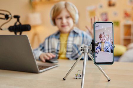 Téléchargez les photos : Focus sur l'écran du smartphone avec un mignon écolier cliquant sur la souris tout en étant assis près des bureaux devant les gadgets et en enregistrant une nouvelle vidéo - en image libre de droit