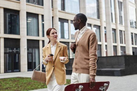 Téléchargez les photos : Jeune femme d'affaires élégante en veste beige et jupe blanche regardant un collègue afro-américain pendant la discussion à la pause café - en image libre de droit
