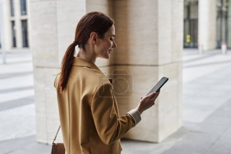 Foto de Joven empleada morena mirando la pantalla del smartphone mientras camina en el entorno urbano y se comunica en el chat de vídeo - Imagen libre de derechos