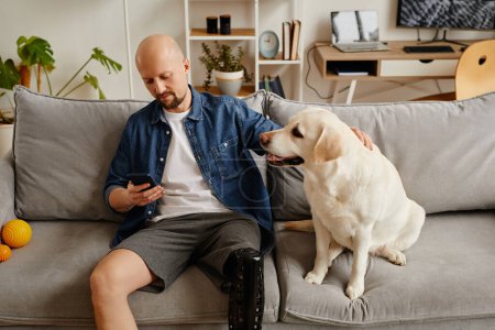 Téléchargez les photos : Portrait de l'homme adulte avec prothèse de jambe relaxant sur canapé et chien blanc caressant - en image libre de droit