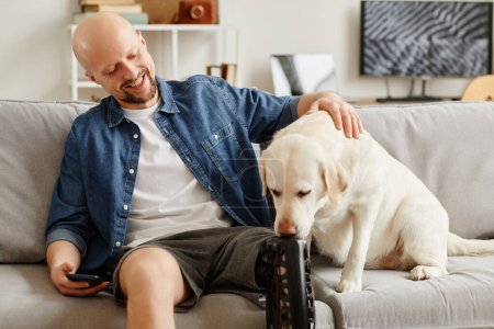 Portrait d'homme adulte souriant avec prothèse de jambe relaxant sur canapé et chien blanc caressant