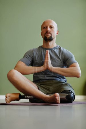 Téléchargez les photos : Homme adulte avec la jambe prothétique appréciant l'entraînement de yoga à l'intérieur et méditant assis en position lotus - en image libre de droit