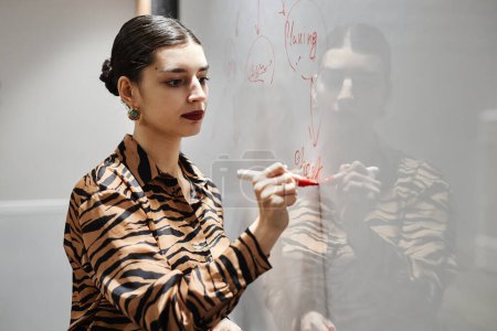 Photo for Waist up portrait of elegant Middle Eastern businesswoman writing on whiteboard while brainstorming ideas in office, copy space - Royalty Free Image
