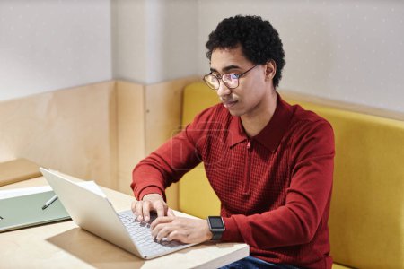 Téléchargez les photos : Portrait de jeune homme du Moyen-Orient portant des lunettes et utilisant un ordinateur au bureau dans une cabine avec éclairage électrique, espace de copie - en image libre de droit